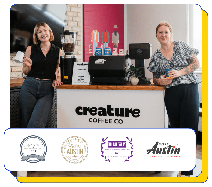 Two baristas standing behind a coffee catering cart counter at Creature Coffee Co with various awards displayed below.