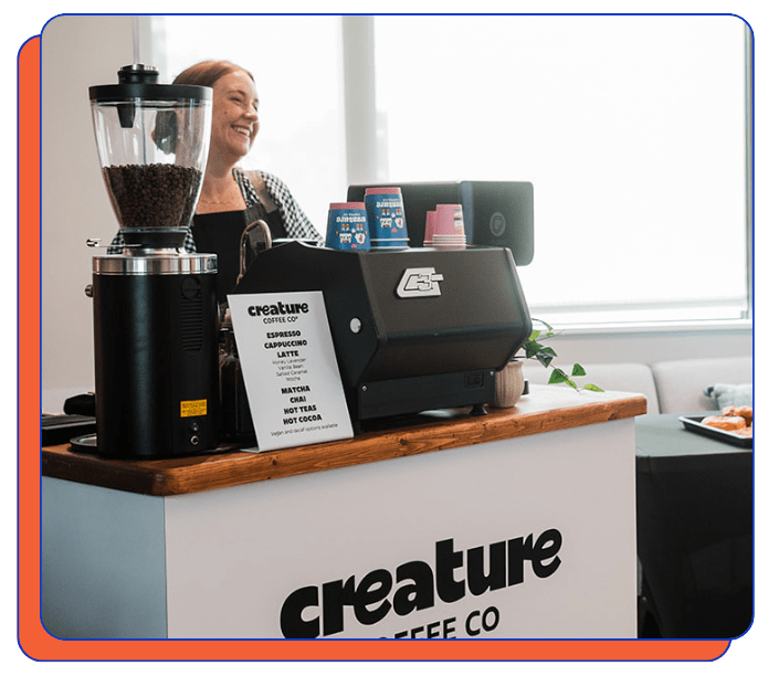 Mobile coffee bar rental counter with coffee grinder, coffee machine, and 'creature coffee co' branding. Coffee catering barista is smiling. 