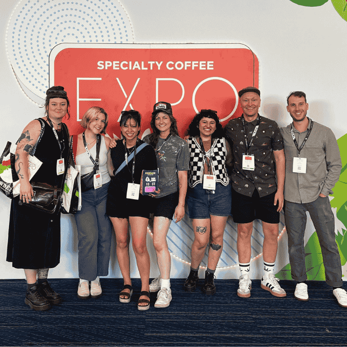 Group of people posing in front of a 'Specialty Coffee Expo' sign.