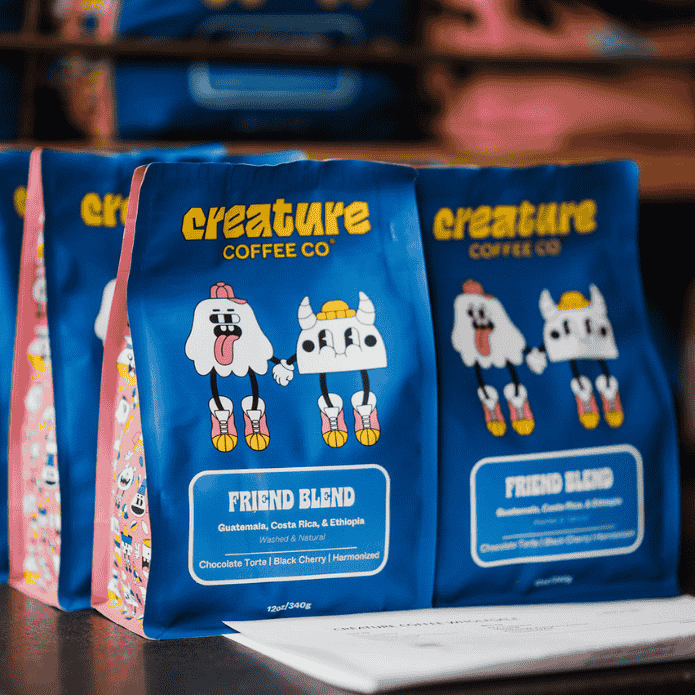Piles of 'creature Coffee Co' coffee bags on a shelf with the brand name displayed on the wall.