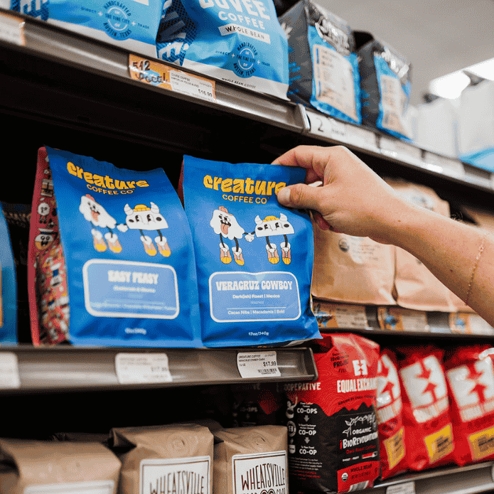 Shelf with blue coffee bags labeled 'creatures' in a store setting