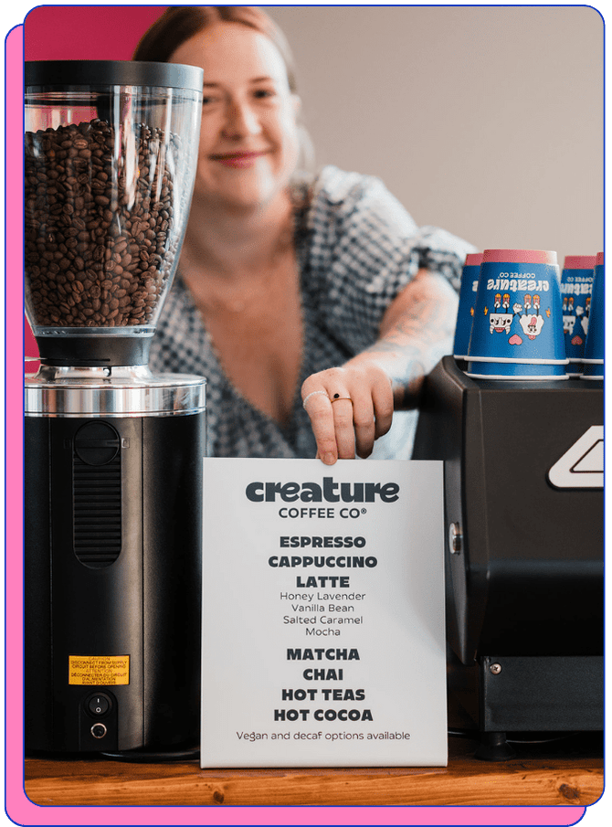 Person behind a coffee grinder with a menu for creature Coffee Co.