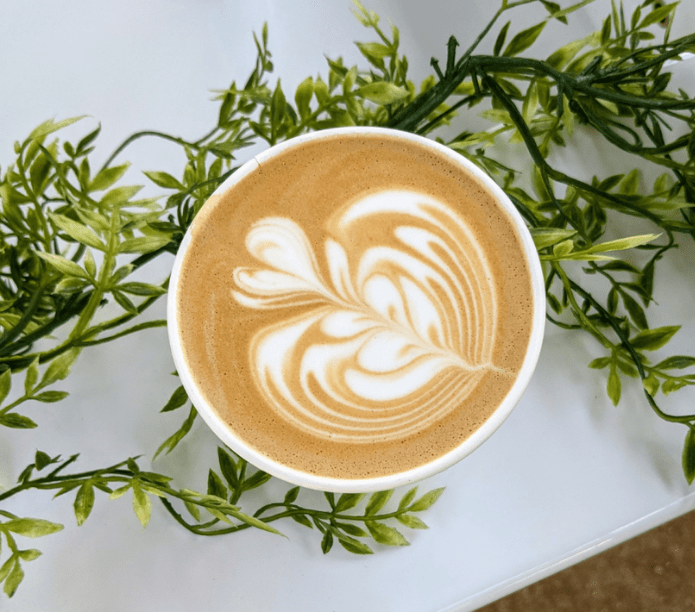 Bad ass latte art from the Creature Coffee baristas. Cup of coffee with latte art on a white surface with green leaves. Event baristas. 