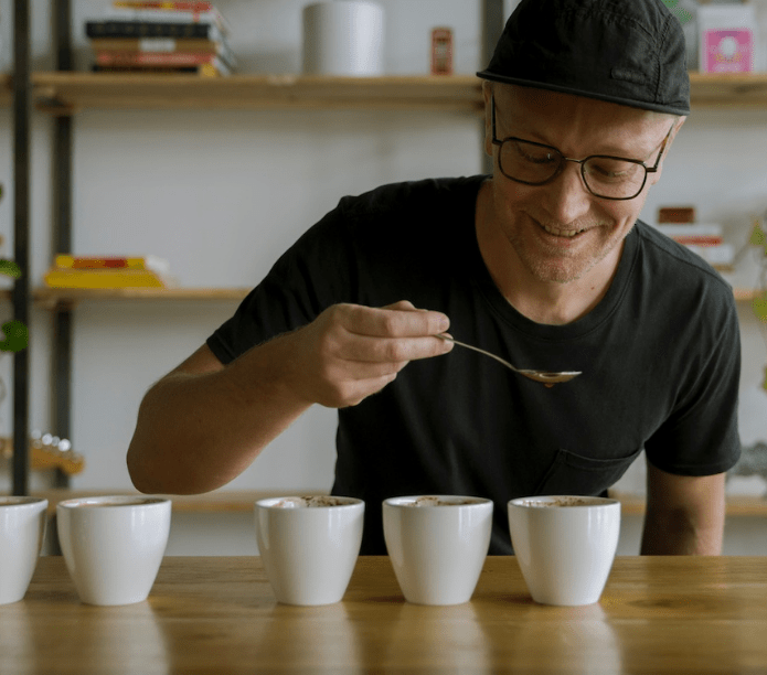 Man tasting coffee from small cups with a spoon in a cozy setting.