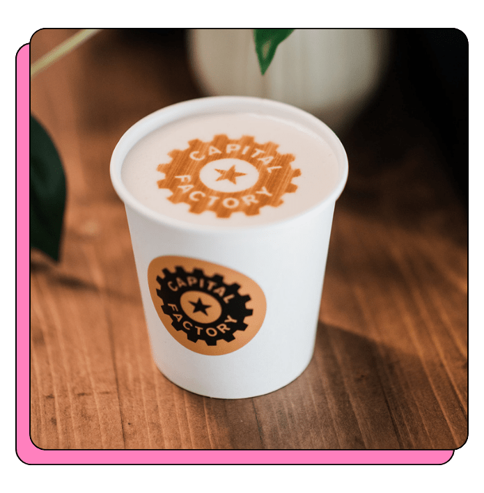 White paper cup with latte printed 'Capital Factory' logo on a wooden surface