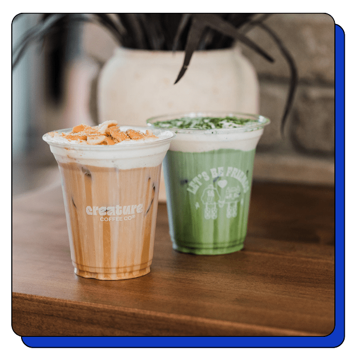 Two Matcha and Iced Latte Cold Foam in clear plastic cups on a wooden surface with a blurred background