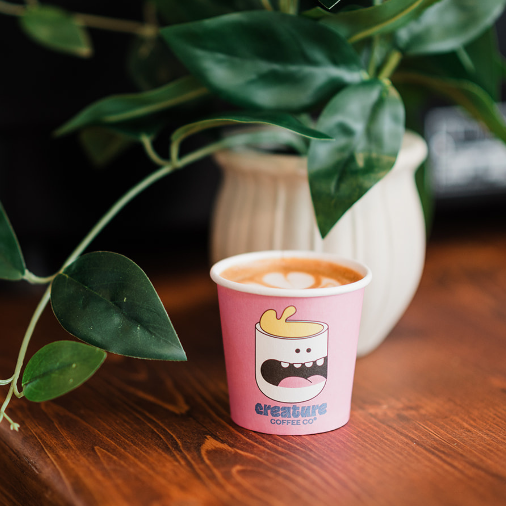 Pink paper cup with a cartoon design on a wooden table with green leaves in the background