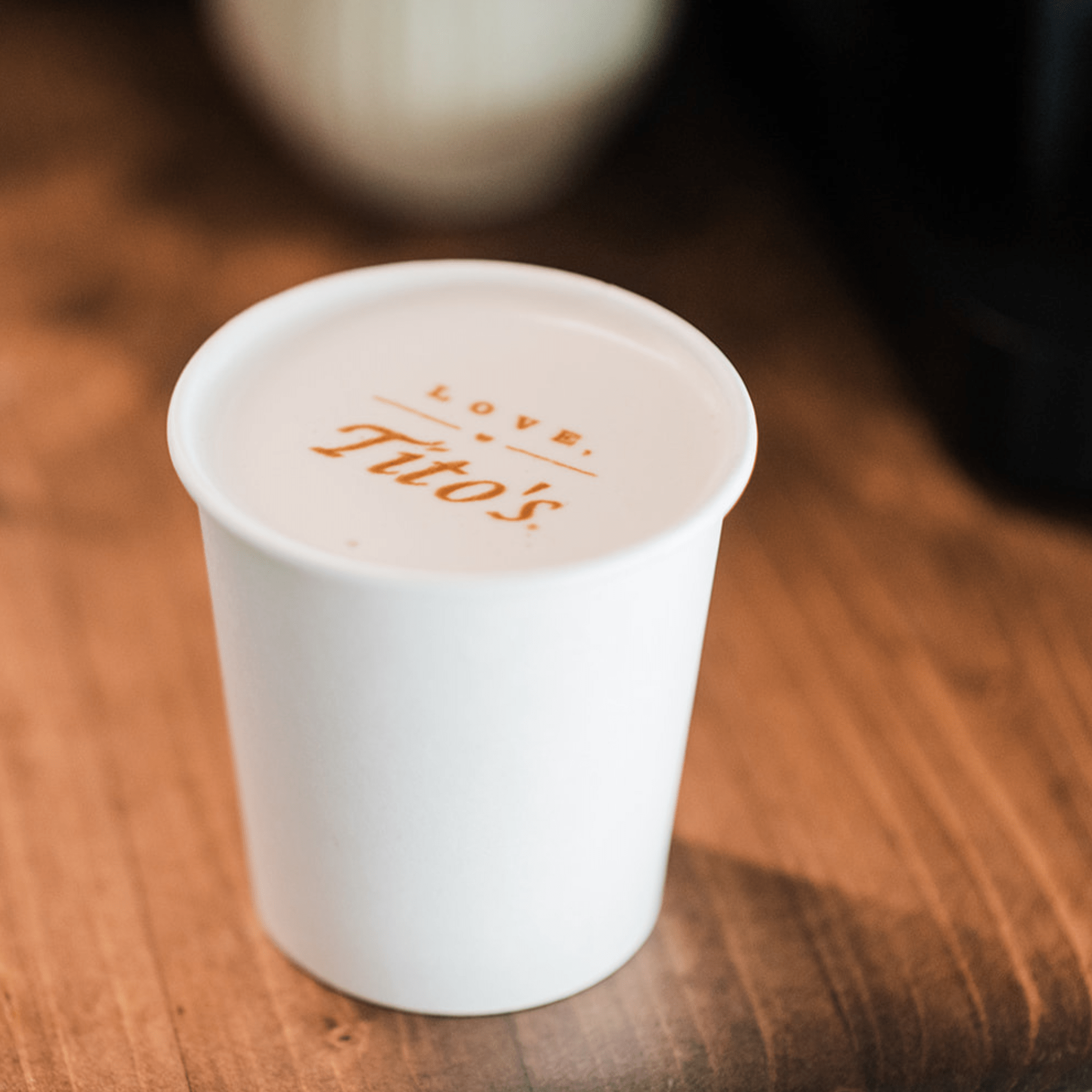 White cup with custom branded latte printing 'Love Tito's' text on a wooden surface