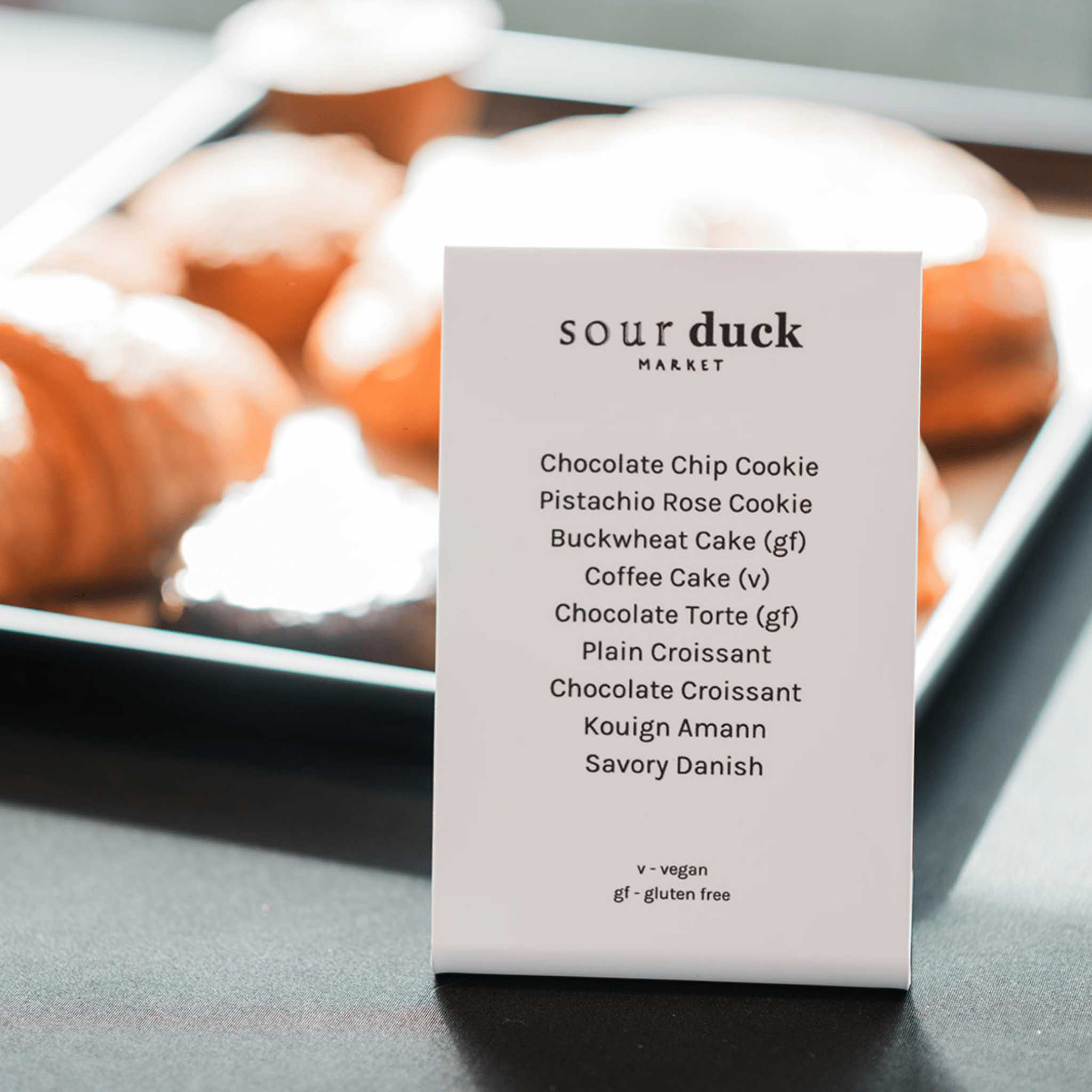 Menu card for Sour Duck Market with dessert options displayed in the background at an event 