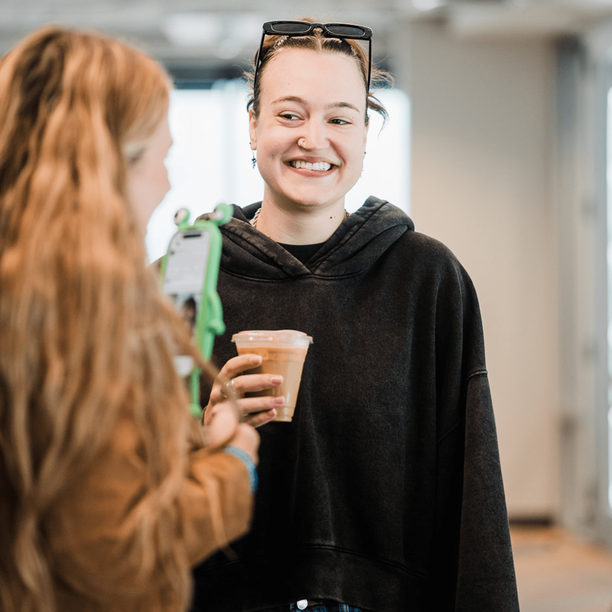 Person holding a coffee catering cup with another person taking a photo in an indoor setting