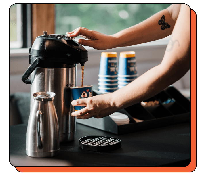 Person pouring coffee from a thermal carafe into a cup on a table.