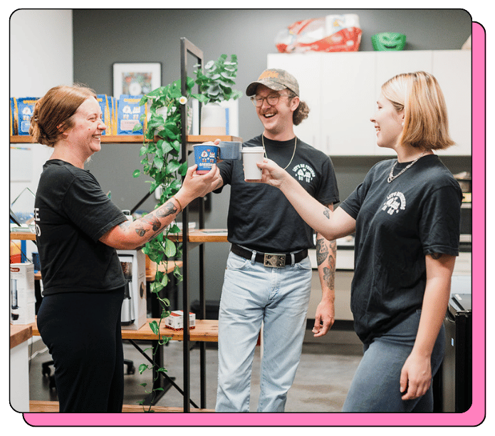 Three people in a casual setting, possibly an office or cafe, with one person handing a cup to another.