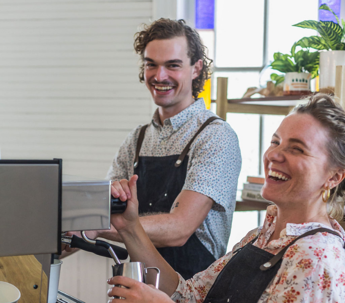 Two Creature Coffee baristas in a mobile coffee shop, both serving a customer with a smile.