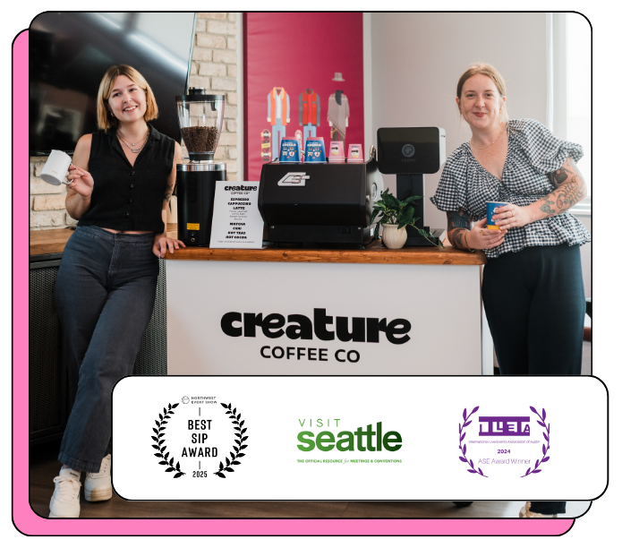 Two baristas standing behind a mobile espresso bar at Creature Coffee Co with awards displayed below.