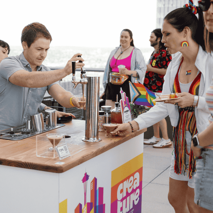 Barista pouring a coffee at a mobile coffee bar with 'creature coffee' branding, surrounded by people in an outdoor setting.