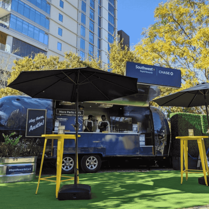 Blue food truck with black umbrella and yellow stools on a city street, custom-branded activation coffee shop experience. 