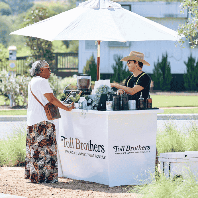 Toll Brothers coffee cart booth with a customer interacting outdoors. Custom-branded coffee shop at event. 