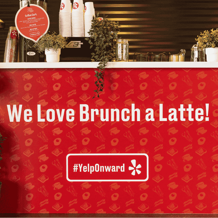 Red Yelp Coffee Cart with 'We Love Brunch a Latte!' text and YelpOnward logo in a coffee shop setting at an event.