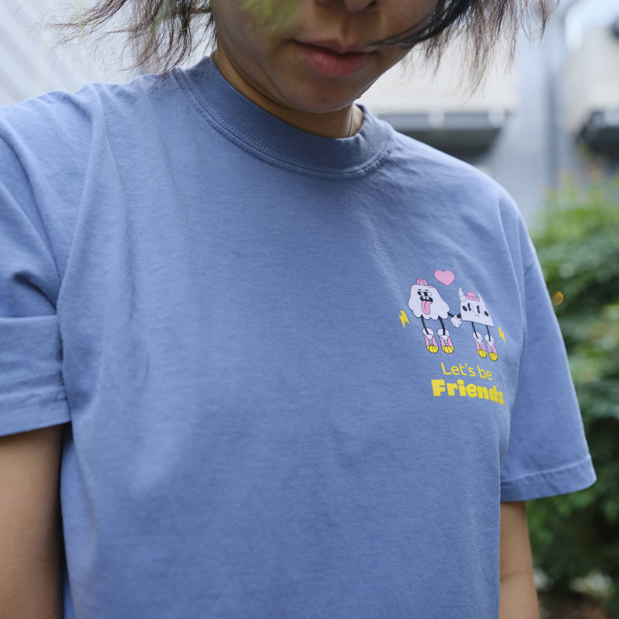 Person wearing a blue t-shirt with cartoon characters and text outdoors, creature coffee.

