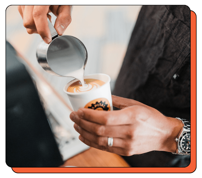 Person pouring milk into a coffee cup with a visible brand logo. Custom-branded mobile coffee cart from Creature Coffee. Silky latte art skills from the best baristas in Austin and Seattle. 