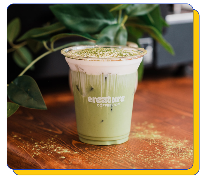 Matcha cold foam iced coffee drink in a clear cup with 'creature coffee co.' branding on a wooden surface.